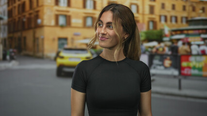 Young blonde woman flexes arm and points forearm with a bright smile in city street; strength...
