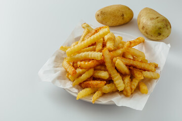 Crispy French Fries Served on White Plate with Fresh Potatoes Next to It