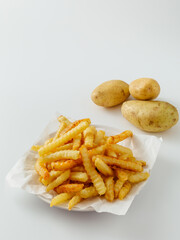 Freshly Cooked Crinkle Cut French Fries and Raw Potatoes on White Surface