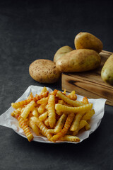 Crinkle Cut French Fries on Paper Plate with Raw Potatoes Background