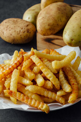 Crispy French Fries Served on White Plate with Fresh Potatoes in Background