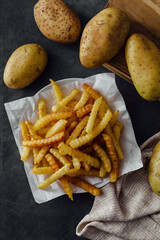 Freshly Cooked Crinkle Cut French Fries on a Dark Background with Potatoes