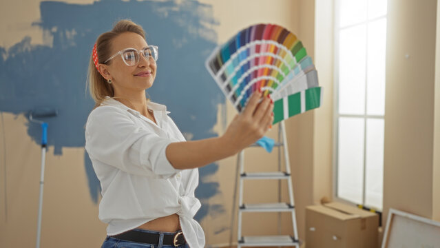 Fototapeta Woman choosing color swatch in newly painted home living room with ladder in background, expressing creativity and style in modern apartment interior.