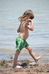 Four-year-old child walking barefoot in the mud on the shore of a lake in sunny South Africa.