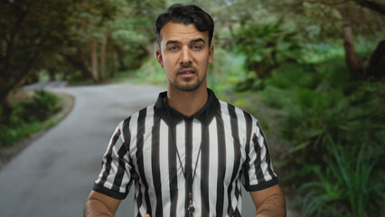 Young hispanic man referee gesturing in park outdoor setting with green surroundings and blurred...
