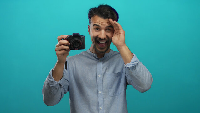 Young man with camera over isolated blue background capturing photos in creative photography scene.
