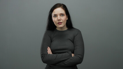 Fototapeta premium Woman with brunette hair and expressive face poses confidently against grey background conveying emotions and gestures while wearing dark long-sleeve top.