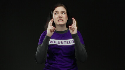 Woman brunette volunteer crossing fingers hoping with a pensive expression against a black...