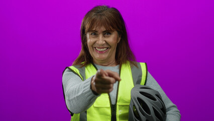 Woman smiling in high visibility vest holding helmet against pink wall background, embodying...
