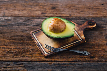 Fresh Sliced Avocado Halved on Wooden Board with Fork Nearby