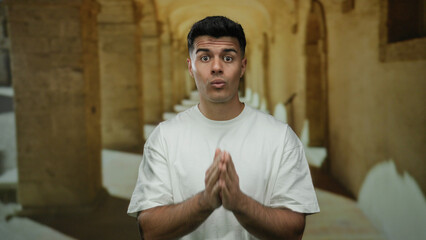 Young man in white shirt standing in historic university corridor conveying emotion.