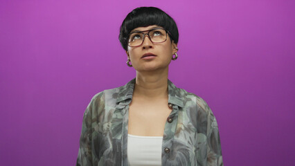 Young chinese woman looking frustrated against a vibrant purple background wearing glasses and a...