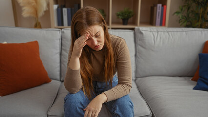 Obraz premium Woman sitting on a couch appears stressed in a modern living room featuring cushions, books, and plants.