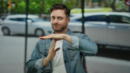 Fototapeta premium Young man with beard makes hand gesture on city street with cars blurred in background during daytime outdoor scene in urban environment