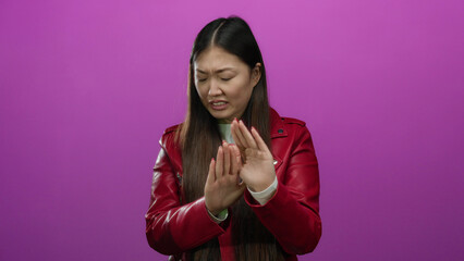 Woman in red jacket showing disgust against an isolated pink background, expressing strong aversion.