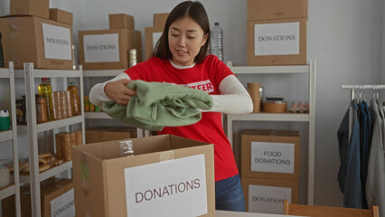 Woman volunteering at donation center sorting clothes among boxes and shelves in a charity room...