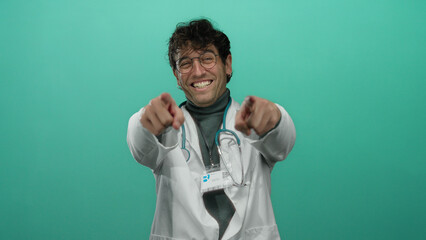 Hispanic doctor with glasses and stethoscope pointing at camera against vibrant green background,...