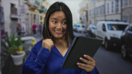 Woman interacting with tablet on city street displaying expressions of surprise and delight in an...