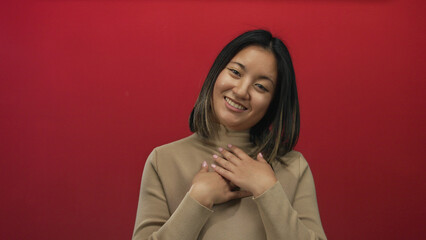Young woman smiling with hands on chest against a vibrant red background expressing happiness and...