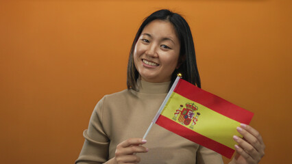 Naklejka premium Woman smiling holding spain flag against orange background showcasing cultural diversity and pride.