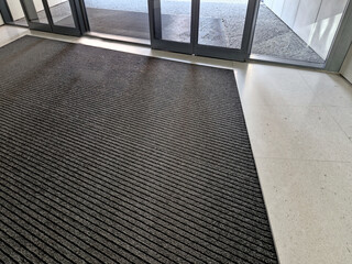 industrial mat cleaning zones at the entrance to the building. A black plastic-metal mat in the shape of an arch or half-circle lies on the limestone mosaic tiles