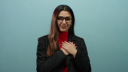 Young hispanic woman in glasses and a black blazer with hands on heart expressing gratitude against...