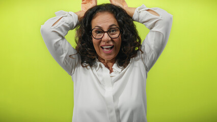 Woman with curly hair making a playful ears gesture on her head against a yellow background,...
