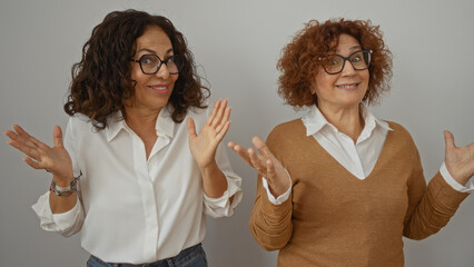 Middle-aged hispanic women gesturing together in a playful manner on a white background, showcasing...