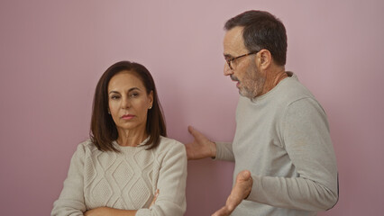 Middle-aged hispanic couple arguing against an isolated pink background depicting a tense family...