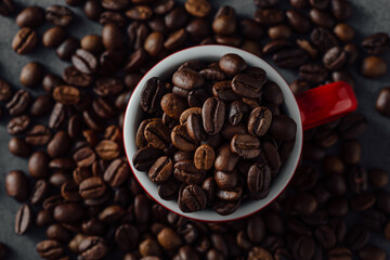Obraz premium Freshly Roasted Coffee Beans in Red Mug Surrounded by Coffee Grounds
