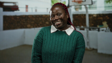 Obraz premium Woman smiling on outdoor basketball court with hoop and fences in the background, wearing a green sweater, showcasing a friendly expression and vivid hair.