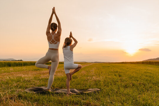Mother and daughter practicing yoga poses in nature.