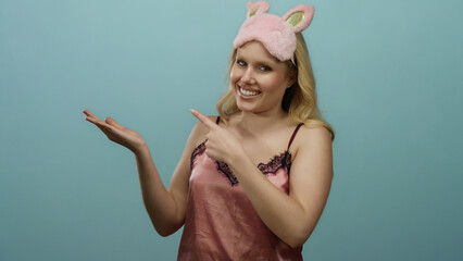 Young blonde woman in pink nightwear with sleep mask smiles against a blue background illustrating...