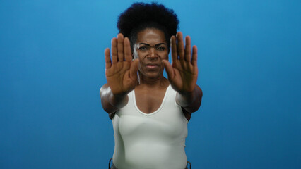 Woman gestures stop with both hands in front of isolated blue background conveying concept of...