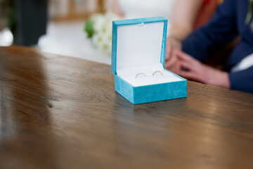 Close up of a blue box with two silver wedding rings on a wooden table, blurred background 