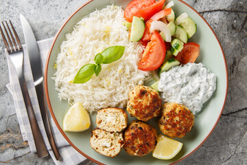 Spicy Greek Chicken meatballs stuffed with feta cheese served with lemon rice, tzatziki sauce and fresh salad close-up in a plate on the table. horizontal top view from above