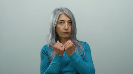 Senior woman with grey hair wearing blue shirt on white background demonstrating punching stance...