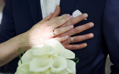 Close up of hands of bride and groom with rings and flowers