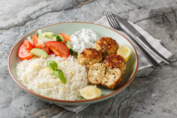 Spicy Greek Chicken meatballs stuffed with feta cheese served with lemon rice, tzatziki sauce and fresh salad close-up in a plate on the table. horizontal