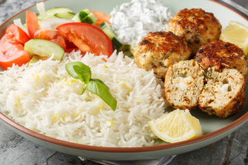 Fried chicken meatballs with sun-dried tomatoes and feta cheese served with lemon rice, tzatziki sauce and vegetable salad close-up in a plate on the table. horizontal