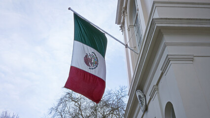 Mexican flag waving outside an embassy building against a clear sky in london, uk, highlighting...