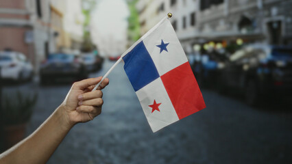 Hand holding panama flag on a bustling city street, highlighting national pride in an urban setting.
