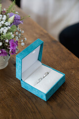 Close up of a blue box with two silver wedding rings on a wooden table, blurred background 