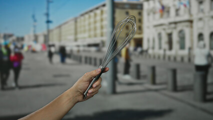 Man holding whisk on city street surrounded by walking people in a vibrant town atmosphere.