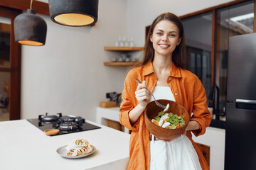 Young woman smiling while holding a salad bowl in a modern kitchen, showcasing healthy eating and...