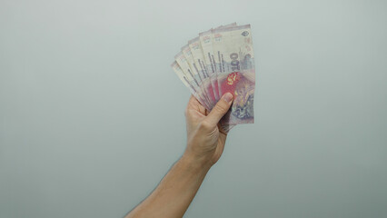 Caucasian male hand holding argentine pesos banknotes against a white isolated background...