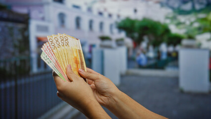 Person holding euro banknotes on a city street, showcasing wealth and investment potential in a...