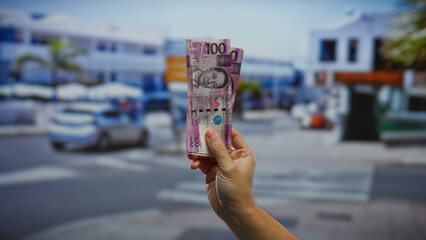 Hand holding philippine pesos on urban street showcasing investment theme with blurred city...