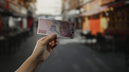 Hand holding turkish lira banknote on city street with blurred urban background, reflecting...