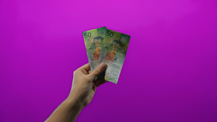 Man holding swiss franc banknotes against a vibrant purple background, depicting economic themes...